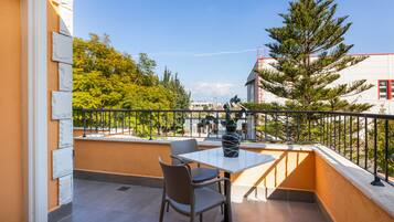 A balcony with a table and chairs, a potted plant, and a view of trees and buildings.