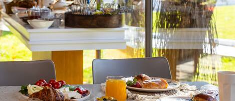 Una mesa de desayuno con diversos platos, entre ellos bollería, frutas y un vaso de zumo de naranja.