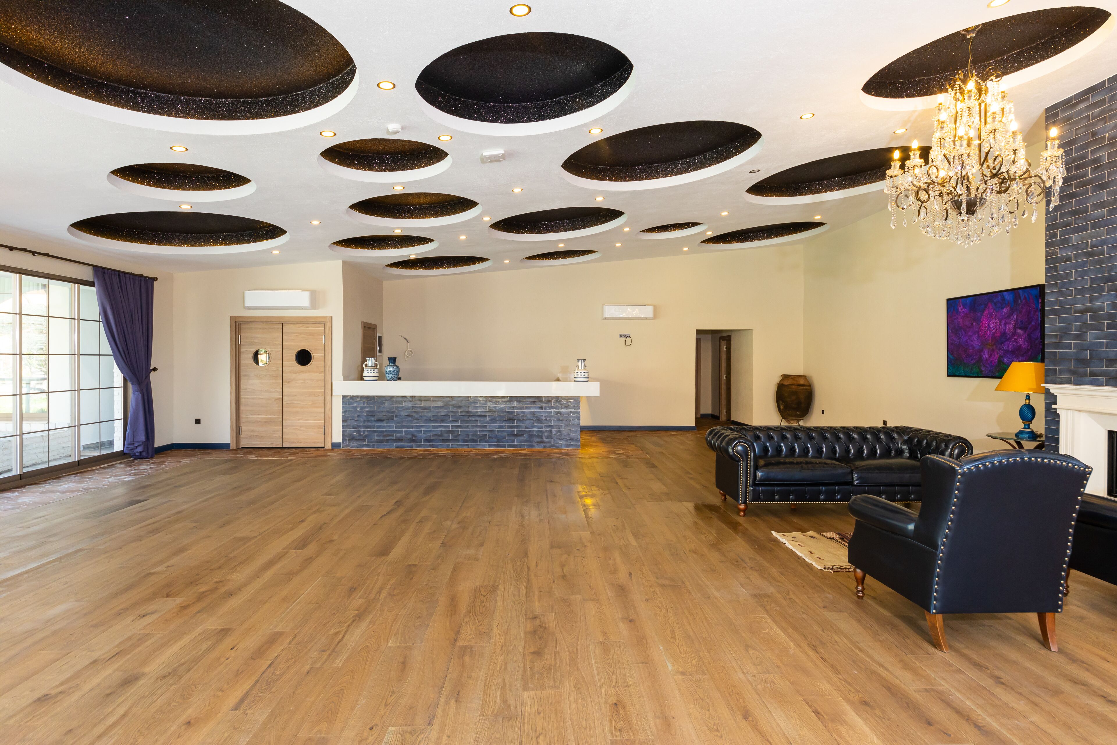 Un vaste espace de vie doté d’un plancher en bois, d’un canapé en cuir noir, d’un lustre et d’une cheminée.