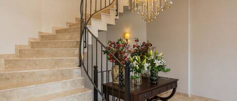 A staircase with a chandelier, a table with flowers, and a wall-mounted lamp.