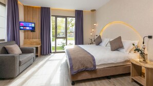A modern hotel room with a large bed, a sofa, a TV, and a view of the outdoors.