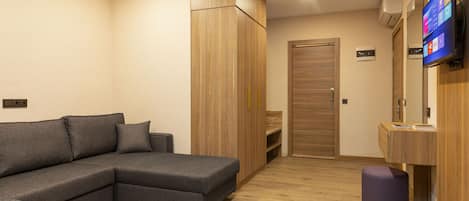 A modern living room with a grey sectional sofa, wooden wardrobe, and a flat-screen TV mounted on the wall.