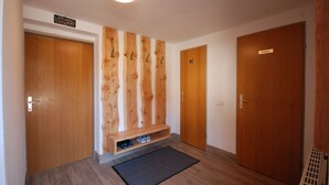 Ein Flur mit Holzwänden, einer Bank mit Schuhen und Türen mit den Aufschriften WC und Privat.