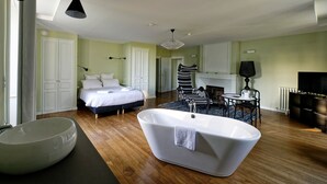 A modern bedroom with a large bed, a freestanding bathtub, and a dining area with a table and chairs.
