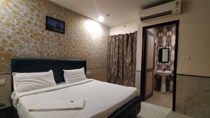 A hotel room with a bed, a nightstand, a wall-mounted TV, an air conditioning unit, and a bathroom visible through an open door. - Redisston Hotel By GRB (Noida)