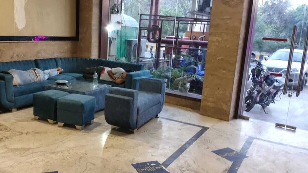 A lobby with a blue sofa set, a coffee table, and a reception desk. - Redisston Hotel By GRB (Noida)