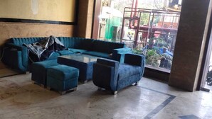 A room with a blue sofa set, a small table, and a desk with papers. - Redisston Hotel By GRB (Noida)