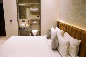 Una habitación de hotel moderna con una cama grande, baño integrado y pared de mármol.