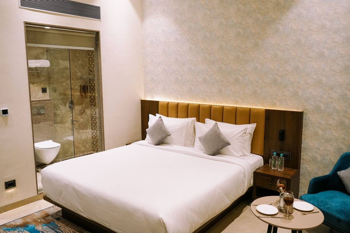 Une chambre d’hôtel avec un grand lit, une douche en verre, une table de chevet avec des bouteilles d’eau et une petite table ronde avec des assiettes et des verres.