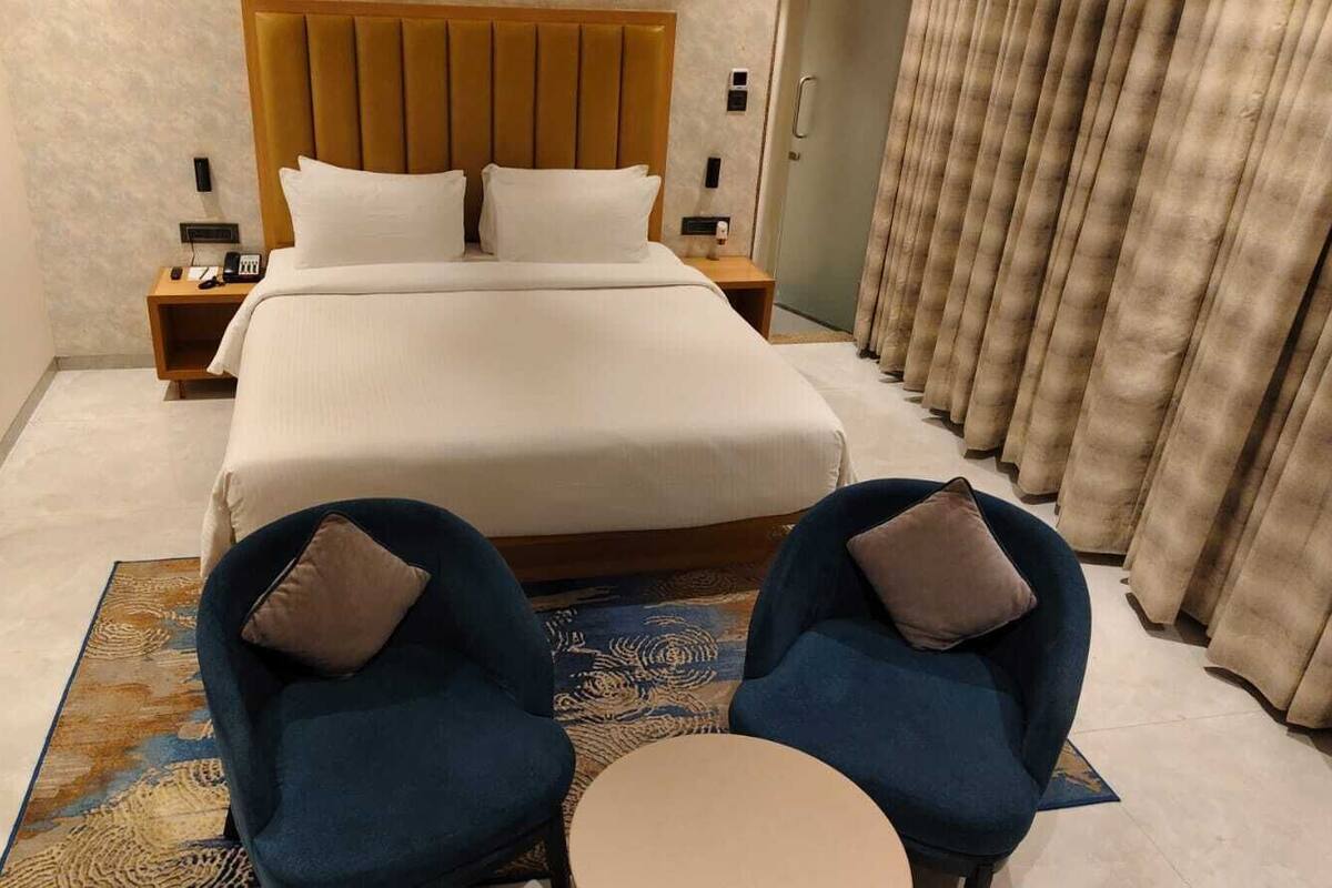 Une chambre d’hôtel avec un grand lit, deux fauteuils, une petite table ronde et une tête de lit ornée de panneaux verticaux.