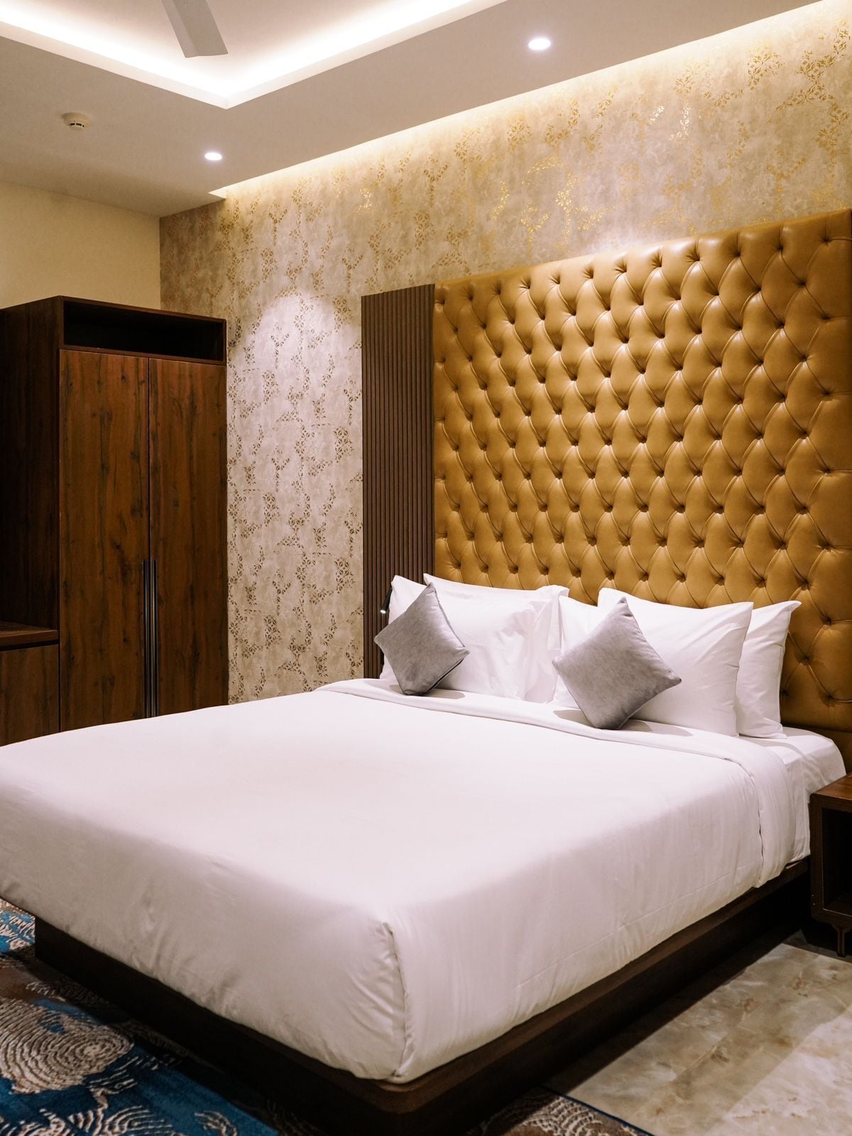 A bedroom with a large bed, a wooden wardrobe, and a decorative headboard.