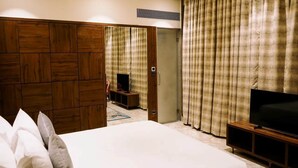 Una habitación de hotel con una cama grande, un televisor sobre un mueble de madera y cortinas en las ventanas.