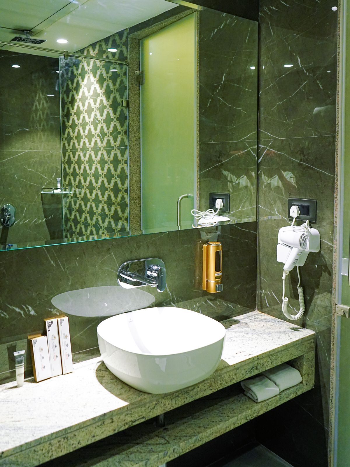 A modern bathroom with a large mirror, a white sink, and a hairdryer mounted on the wall.