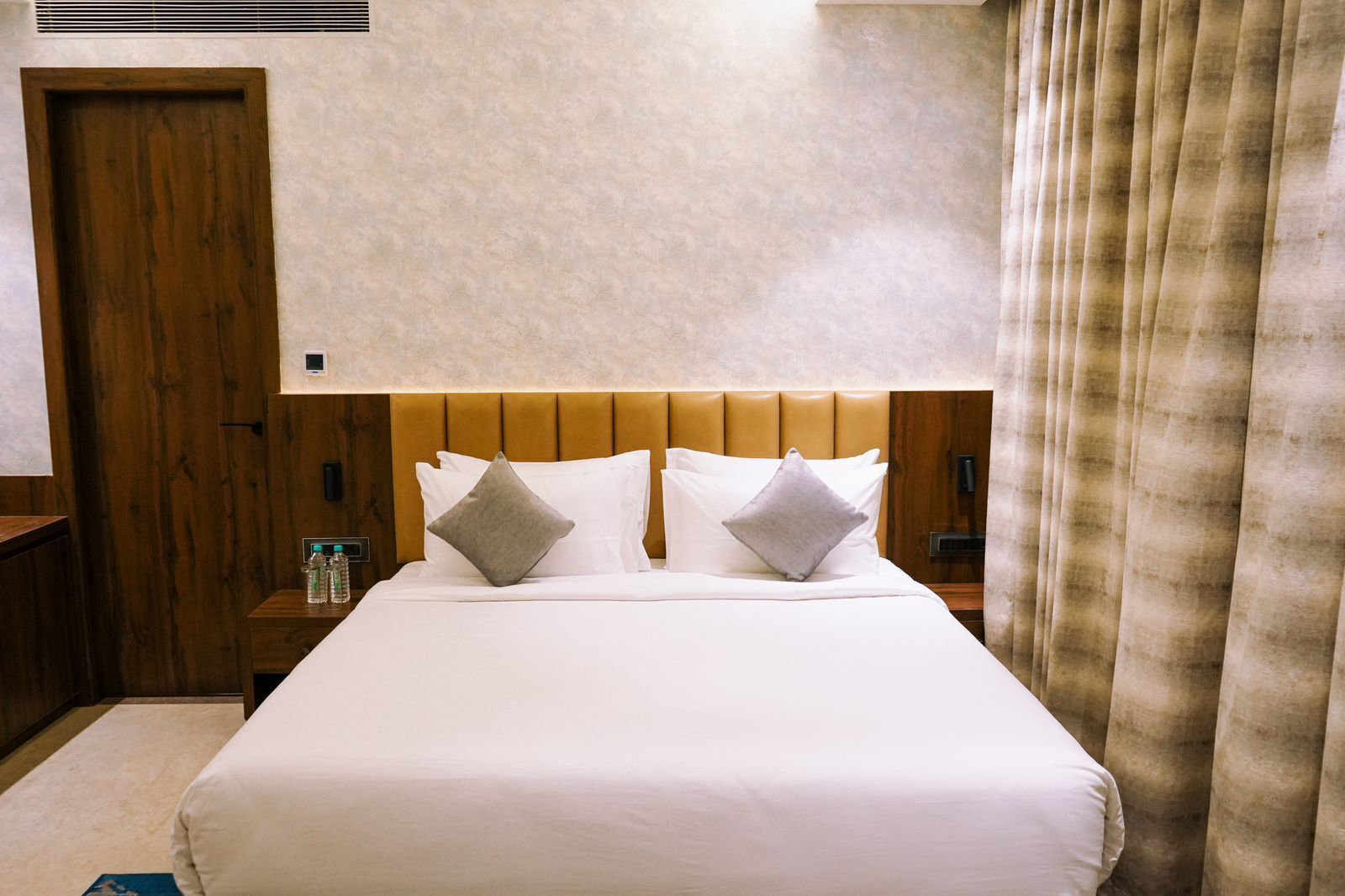 Habitación de hotel con una cama grande, cabecero de madera, dos mesitas de noche y una cortina.