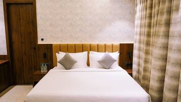 Habitación de hotel con una cama grande, cabecero de madera, dos mesitas de noche y una cortina.