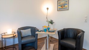Een kamer met twee leren stoelen, een kleine tafel met een bloevas, en een schilderij aan de muur.