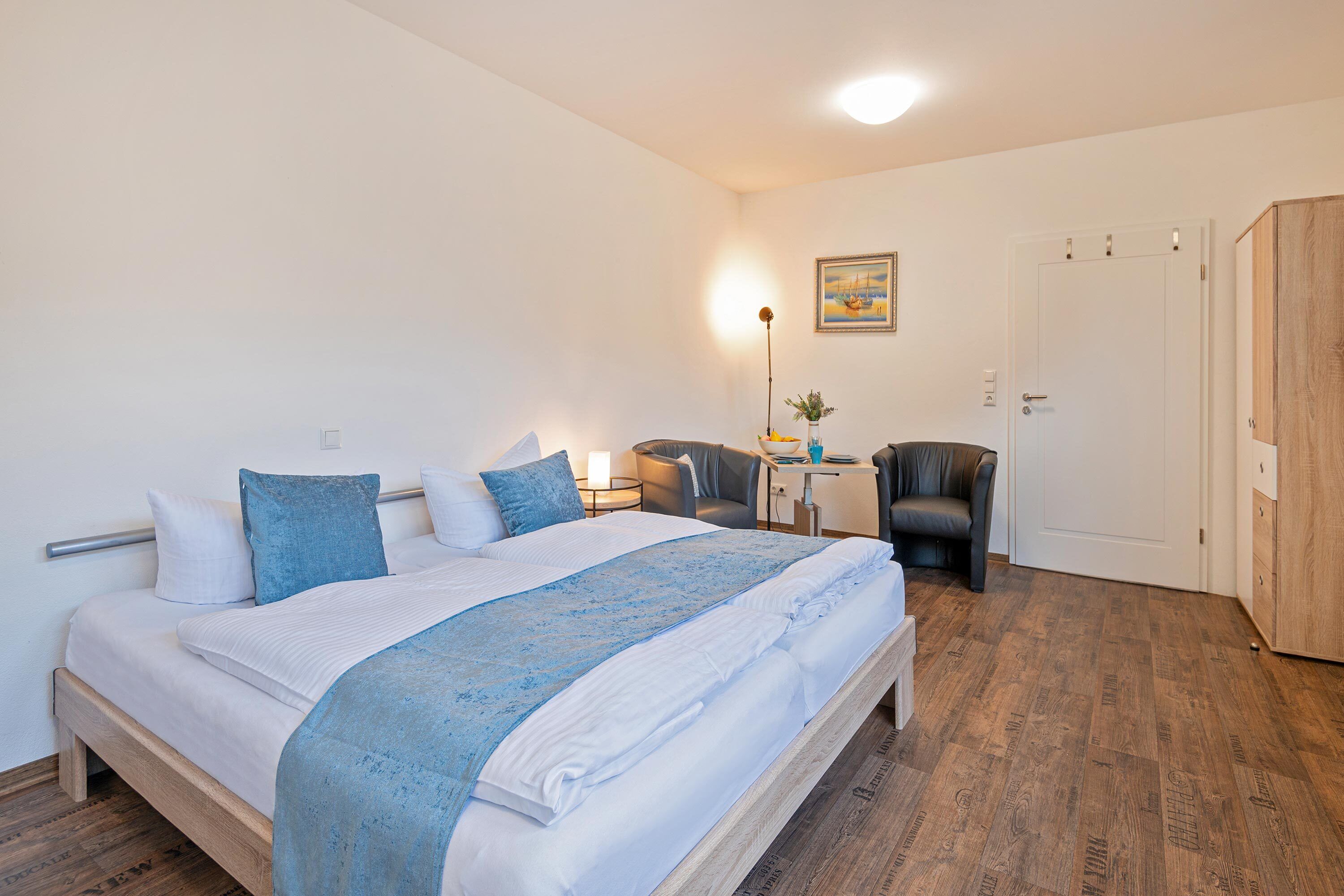 Ein ordentlich eingerichtetes Schlafzimmer mit Bett, Nachttisch, Lampe und einem Sessel.