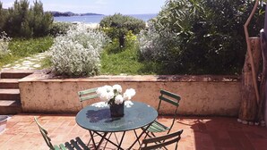 Una terrazza esterna con un tavolo rotondo e quattro sedie, immersa nel verde e con vista sul mare.
