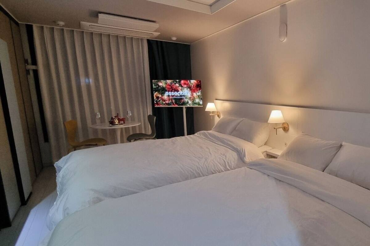 A hotel room with two beds, a TV on a stand, a small table with a chair, and a window with curtains.