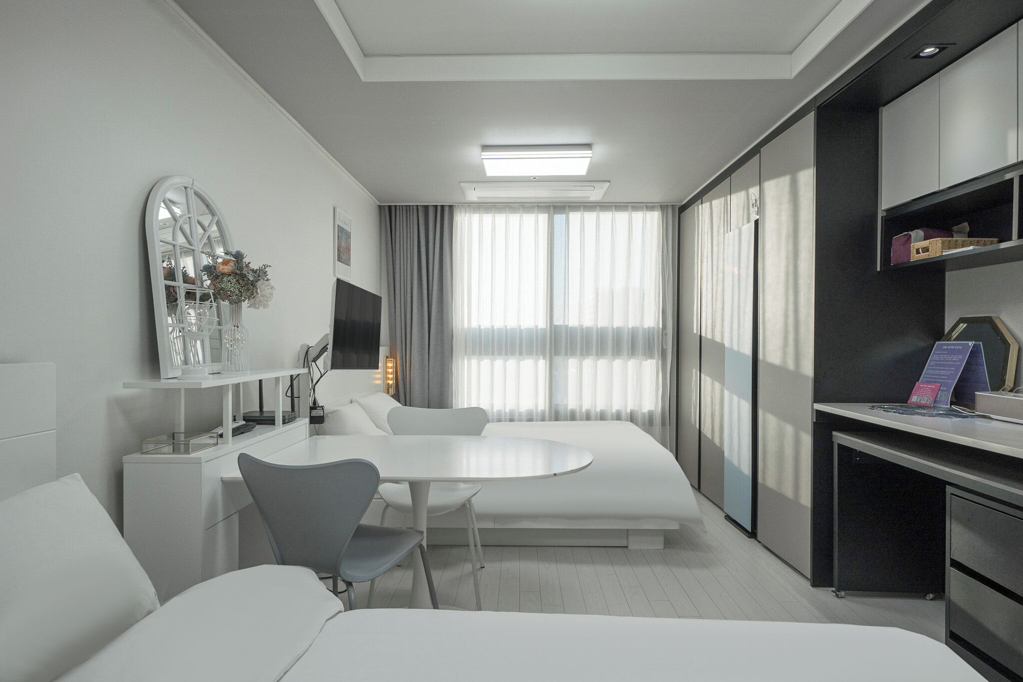 A modern hotel room with a round dining table, a sofa, a desk, and a large window with curtains.