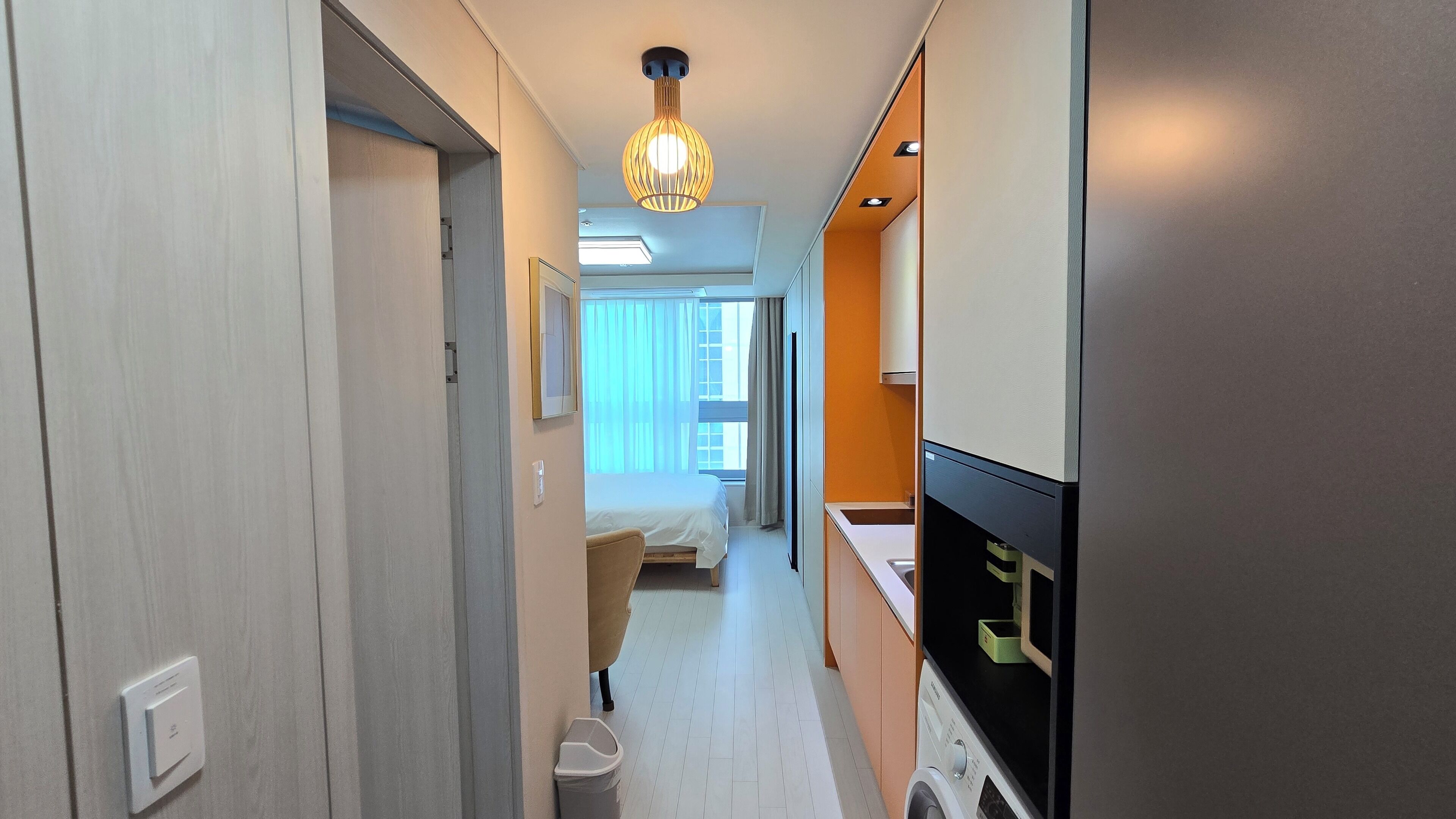 En hotellkorridor med en säng, en stol, en tvättmaskin och en tv.