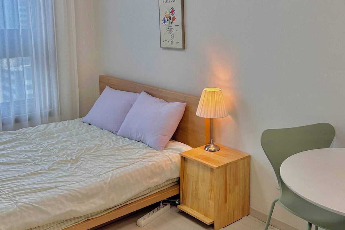 A neatly made bed with a wooden headboard, a bedside table with a lamp, a small round table, and a chair.