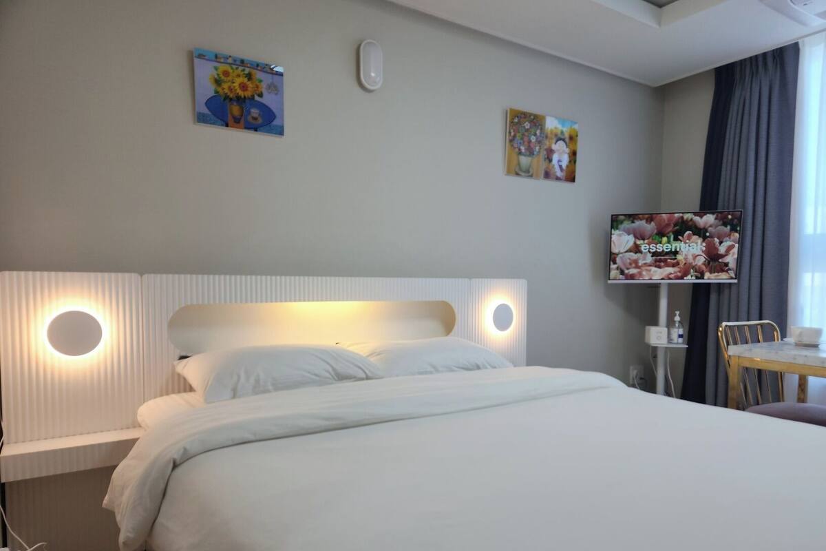 A hotel room with a bed, bedside table, TV, and artwork on the walls.