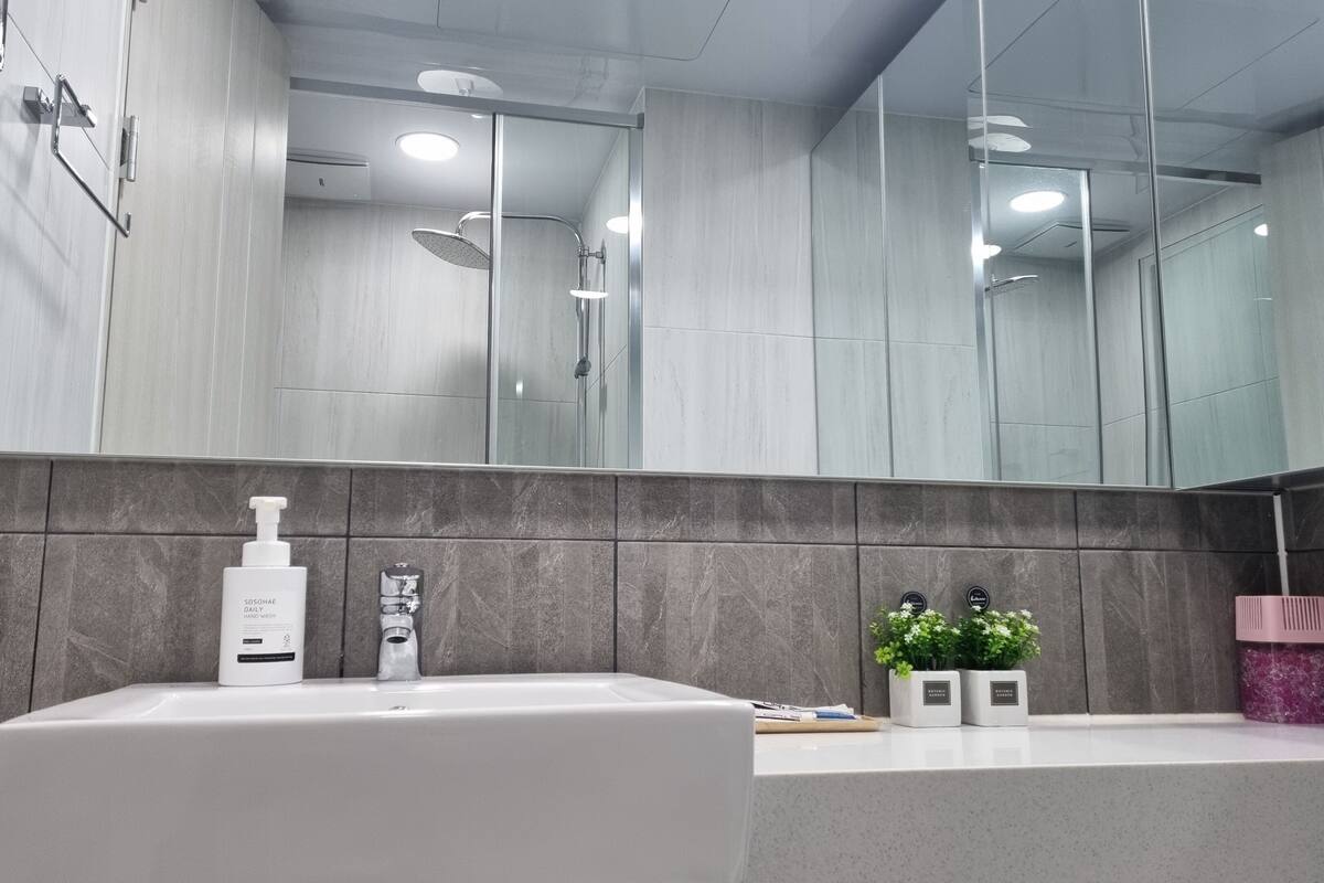 A modern bathroom with a large mirror, a sink, and a shower area.