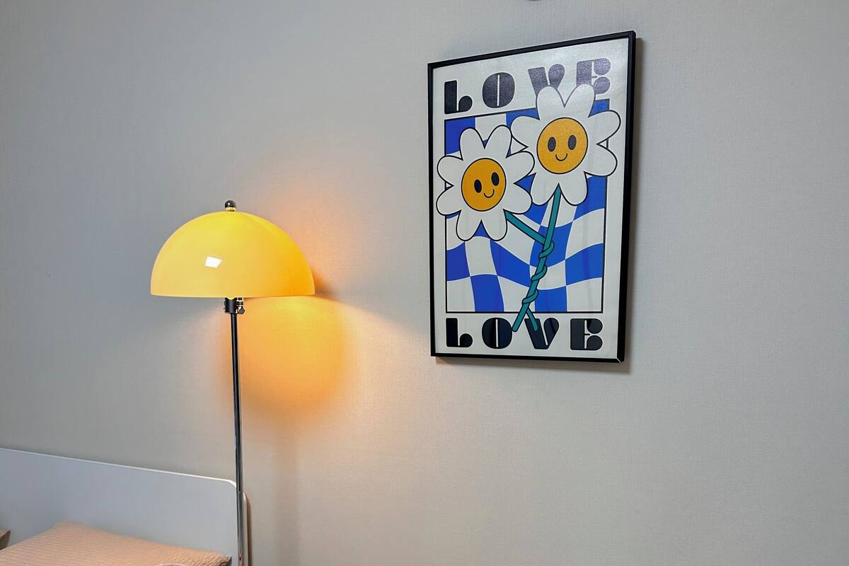 A room with a grey sofa, a yellow floor lamp, a glass table with a decorative item, and a wall with a 'LOVE' poster.
