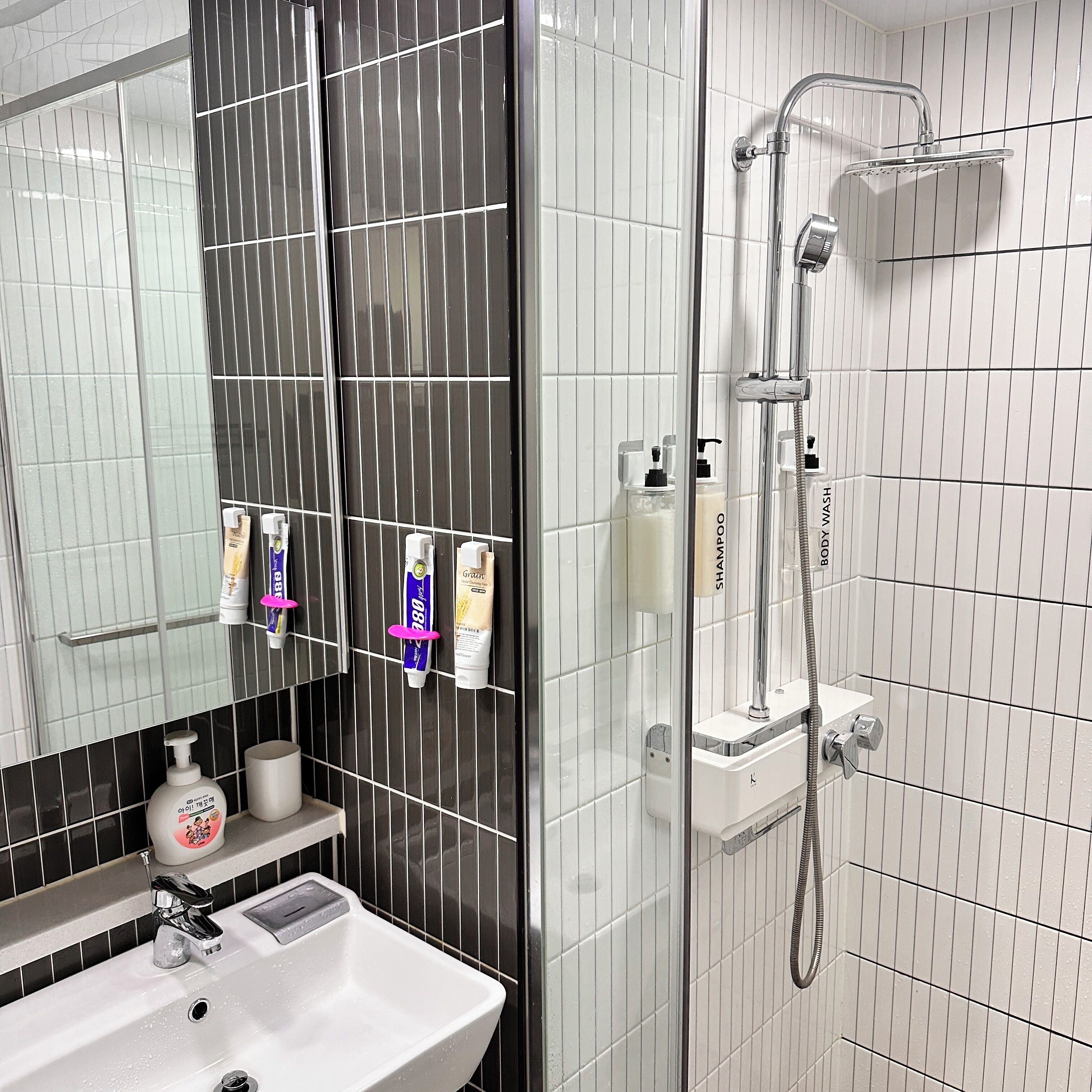 A modern bathroom with a white sink, black and white tiled walls, a glass shower enclosure, and toiletries on a rack.