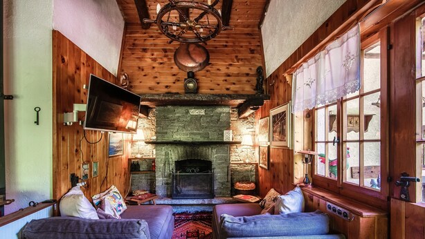 A cozy room with a stone fireplace, wooden walls, and a television mounted on the wall. - Casa al Fiume (Sonogno)