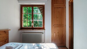A bedroom with a wooden headboard, a window with a view of greenery, a radiator, and a neatly made bed with towels. - Casa al Fiume (Sonogno)