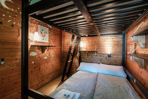 A wooden cabin room with a bed, a ladder, and a wall-mounted shelf.