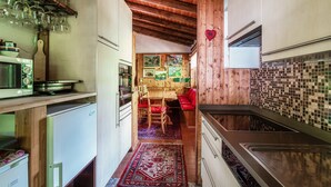 A narrow kitchen with wooden beams, a dining area with red chairs, and a tiled backsplash. - Casa al Fiume (Sonogno)