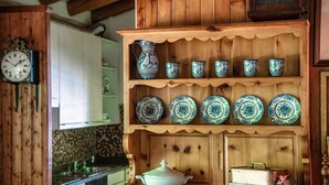 A kitchen with wooden cabinets, a clock, and a shelf with ceramic dishes. - Casa al Fiume (Sonogno)