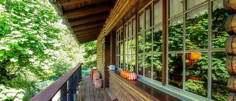 A wooden porch with a railing, large windows, and a view of greenery.