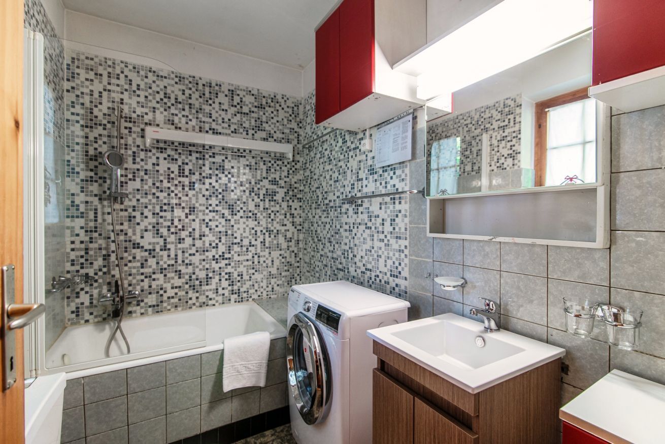 Un baño moderno con pared de mosaicos, lavadora, bañera y lavamanos con un espejo arriba.