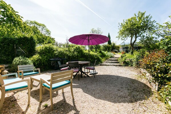 Un espace extérieur aménagé avec une table et des chaises, un parasol violet et un chemin de gravier.