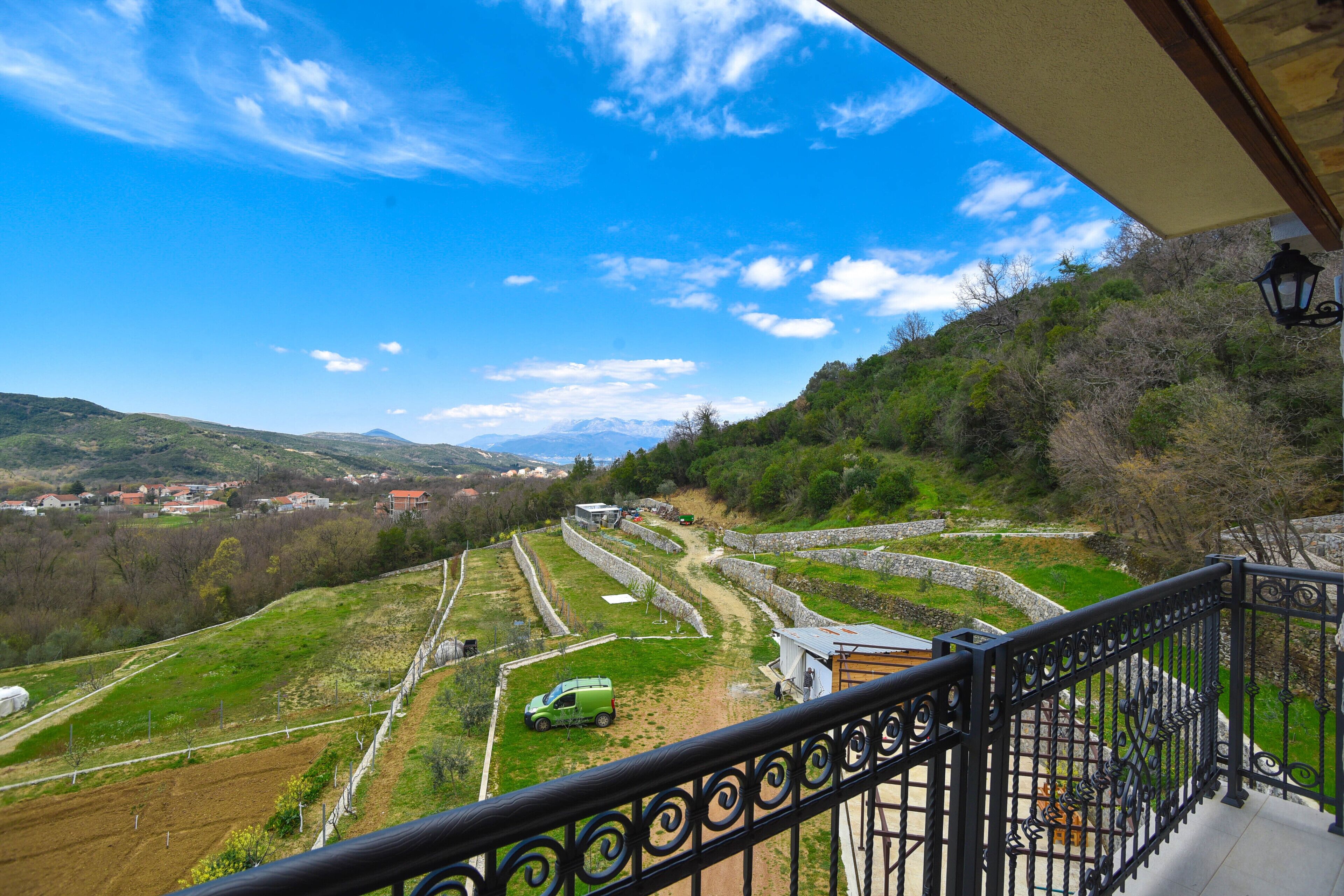 Un balcón con vistas a un paisaje rural, que incluye campos, un coche verde y edificios a lo lejos.