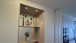 A modern kitchen with built-in appliances, a wooden shelf unit, and a red bench. - Appart Avec Terrasse vue Plage, 2 Minutes du Centre, 2 Vélos et Linge Fournis (Arcachon)