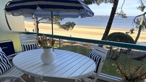 A deck with a white table and chairs, a striped umbrella, and a view of the beach. - Appart Avec Terrasse vue Plage, 2 Minutes du Centre, 2 Vélos et Linge Fournis (Arcachon)