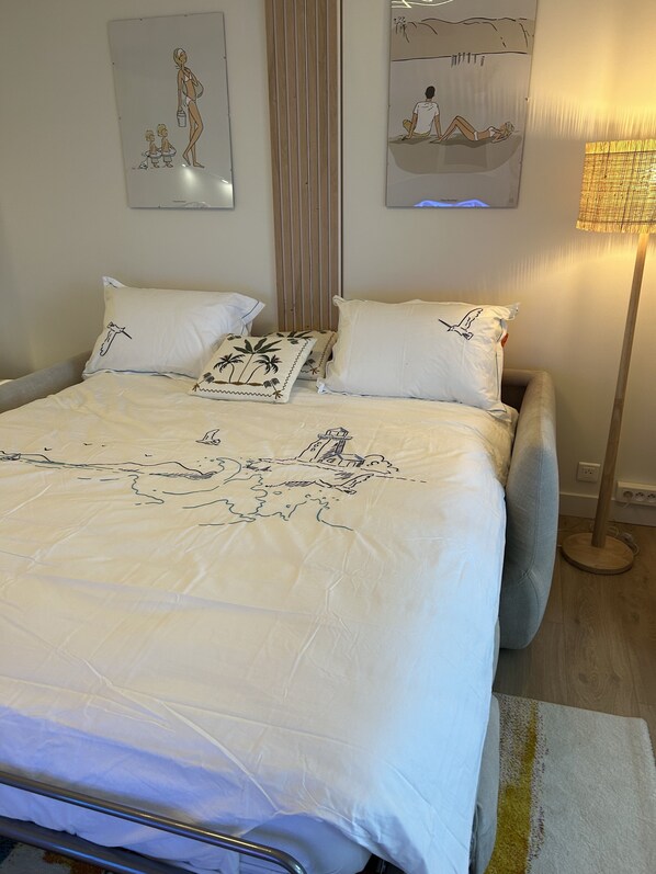 A neatly made bed with a white bedspread featuring a landscape design, flanked by two pillows with bird illustrations. - Appart Avec Terrasse vue Plage, 2 Minutes du Centre, 2 Vélos et Linge Fournis (Arcachon)
