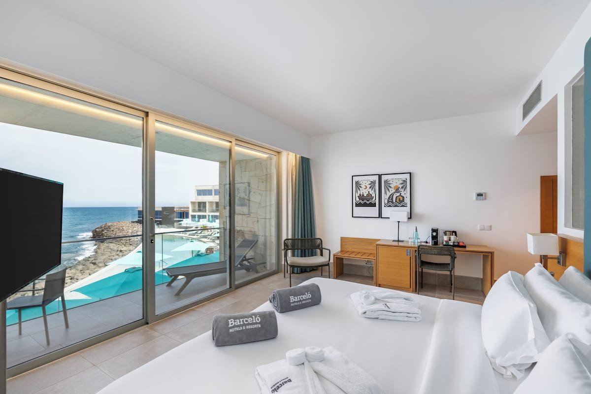 Habitación de hotel con cama, escritorio, silla, televisión y vista al océano.