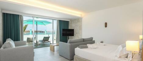 A hotel room with a bed, two armchairs, a sofa, a TV, and a view of the ocean.