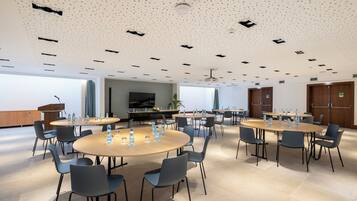 A conference room with multiple tables and chairs, equipped with water bottles and glasses, and a large screen on the wall.