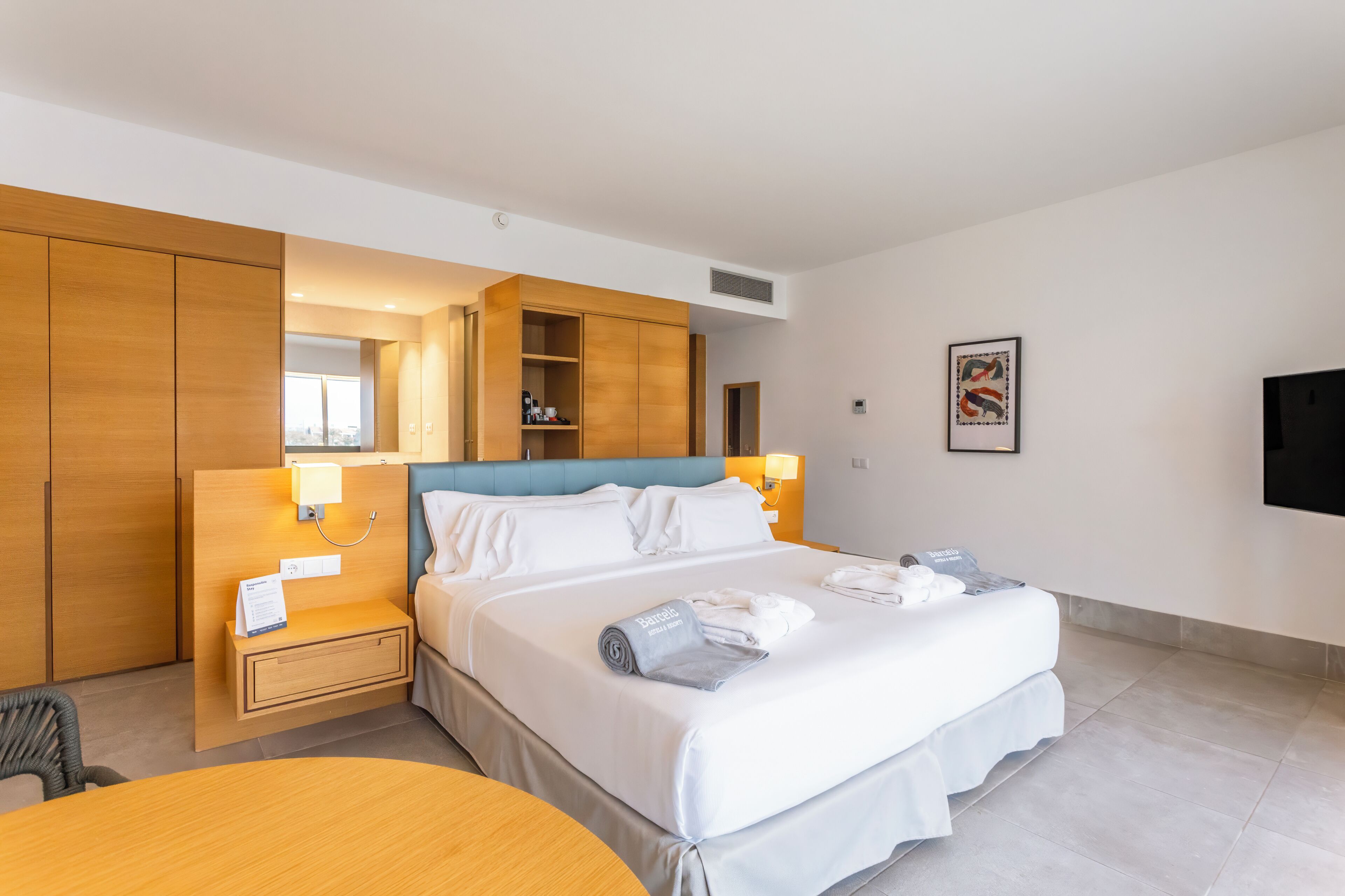 A hotel room with a bed, bedside table, lamp, and a wall-mounted TV.