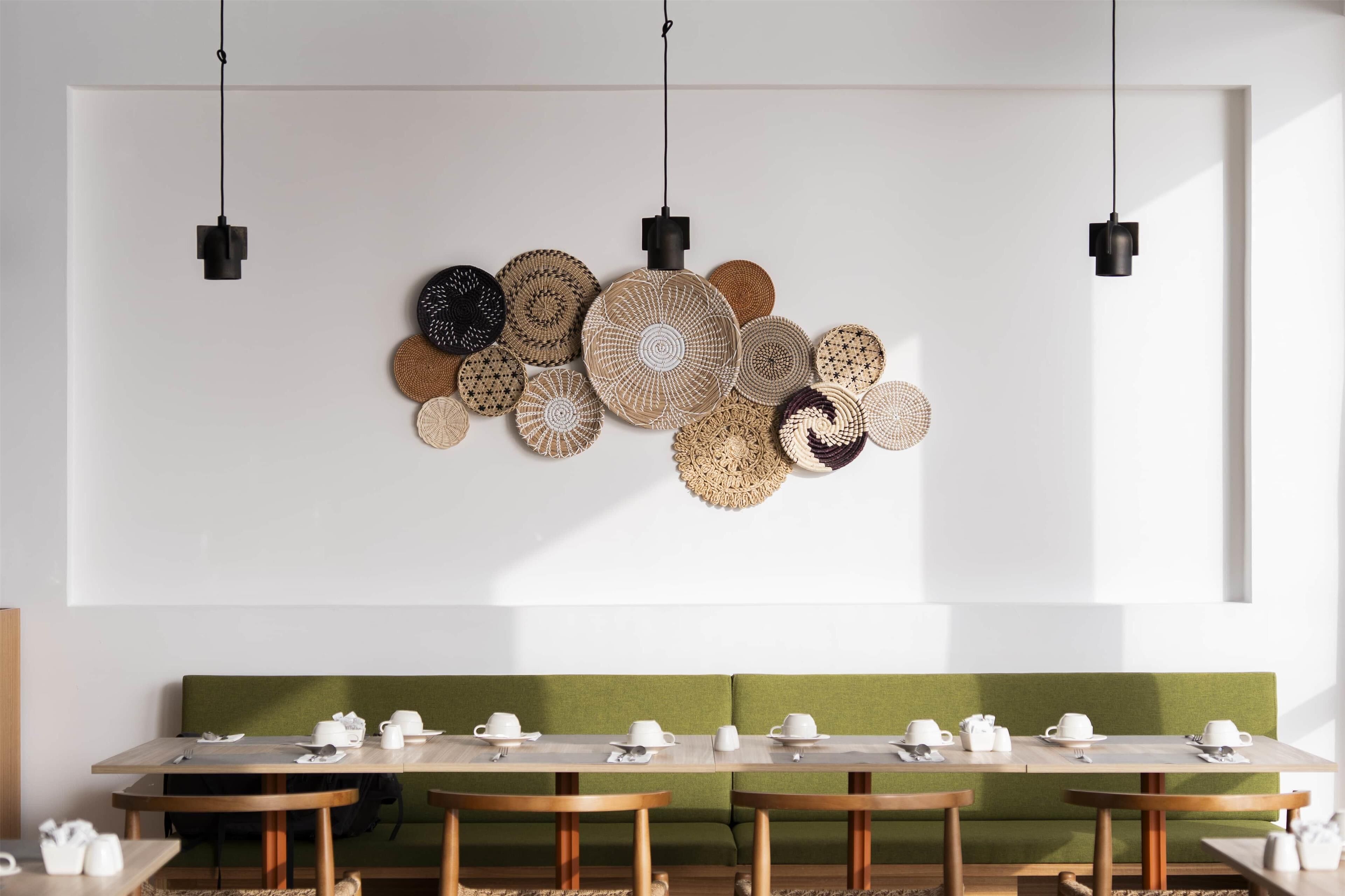 Een eetgedeelte met een lange tafel, een groene gewatteerde bank en wanddecoratie van geweven materiaal.