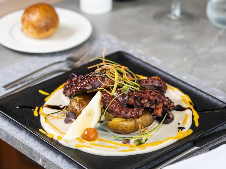 Un plato con pulpo, limón y adornos sobre un plato negro.