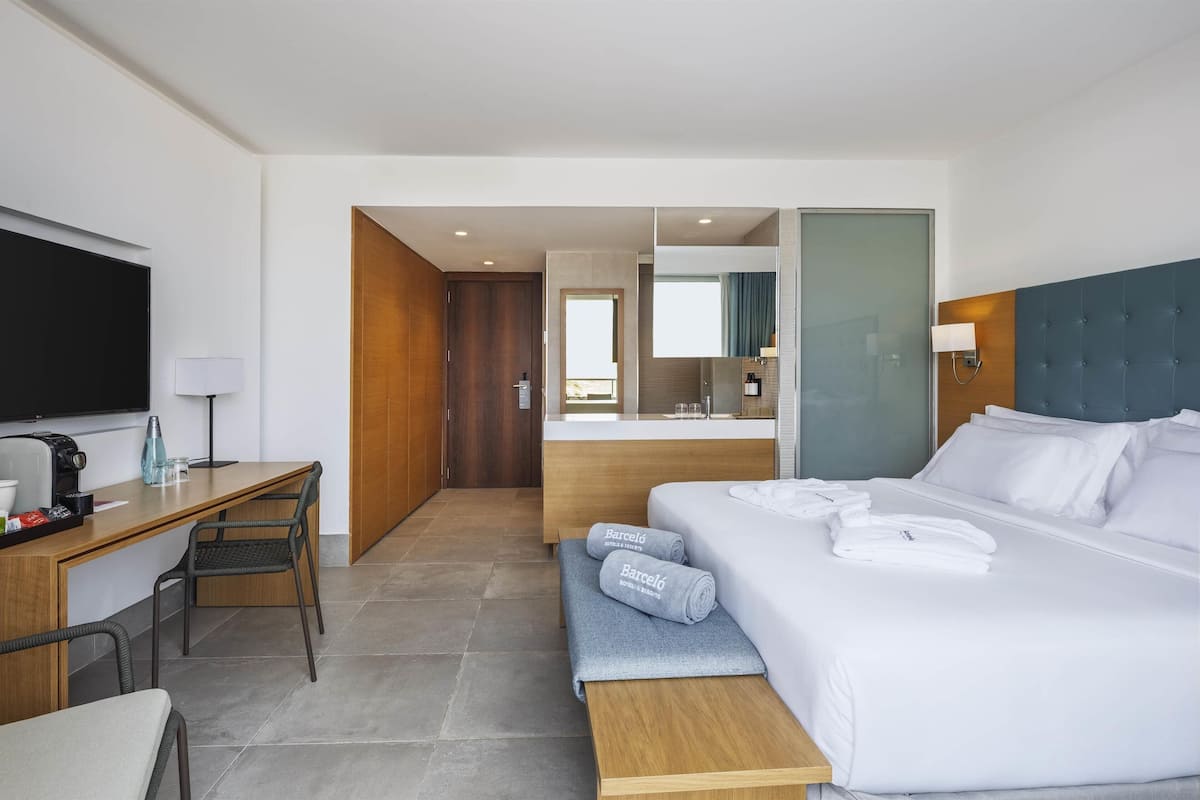 A modern hotel room with a bed, a desk, and a seating area.