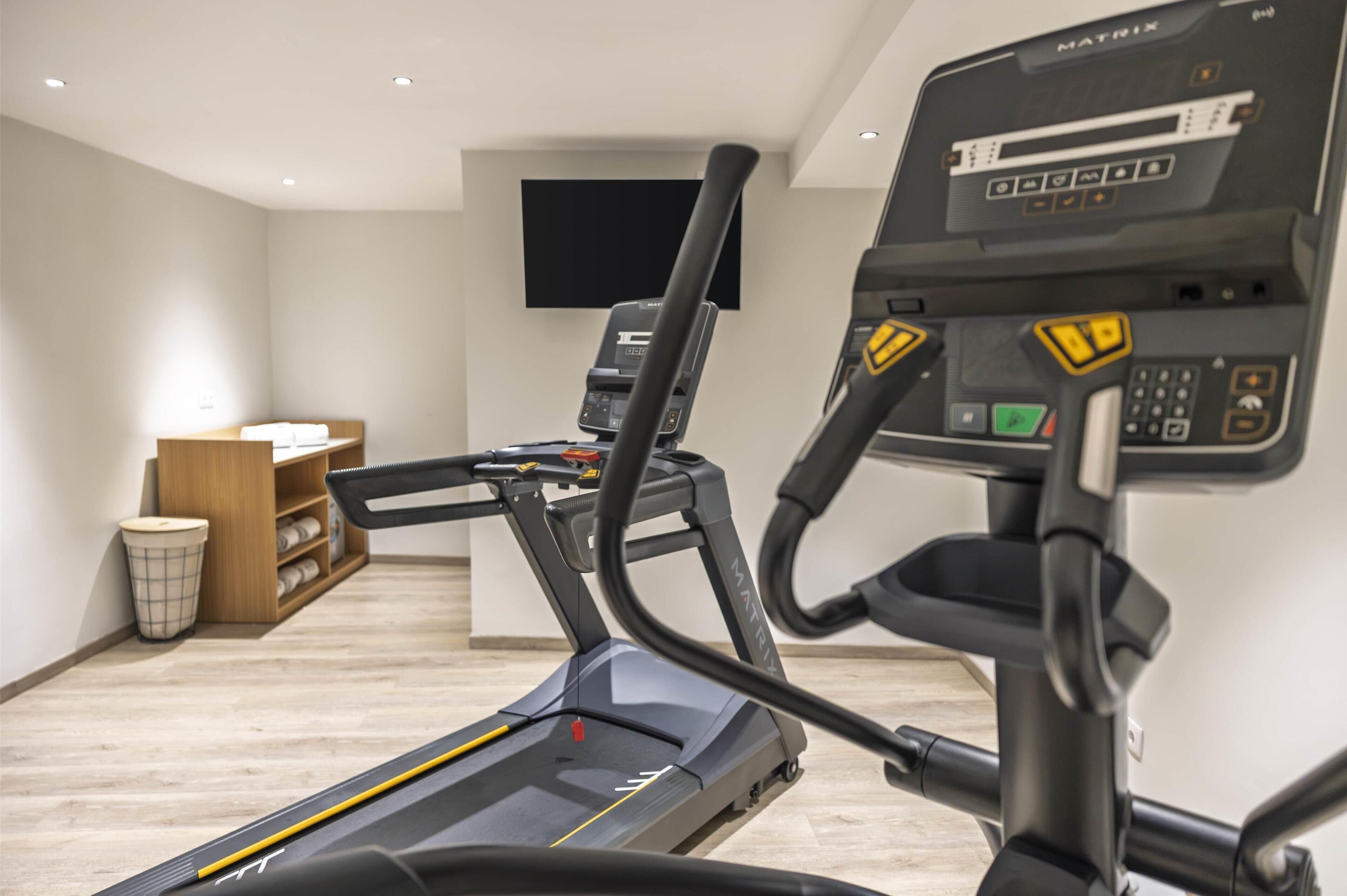 A home gym with a treadmill, a stationary bike, and a wall-mounted TV.